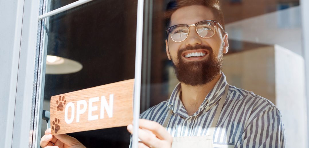 smiling man placing an open sign on a cafe window