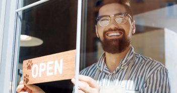 smiling man placing an open sign on a cafe window