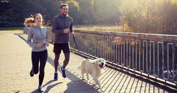 Couple jogging with their dog on a leash along a paved path in early fall