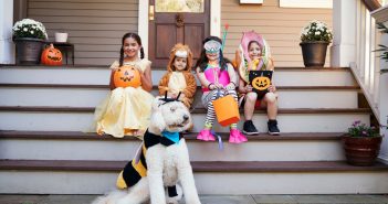 Dog wearing a bumble bee costume in front of four children in Halloween costumes on a porch.